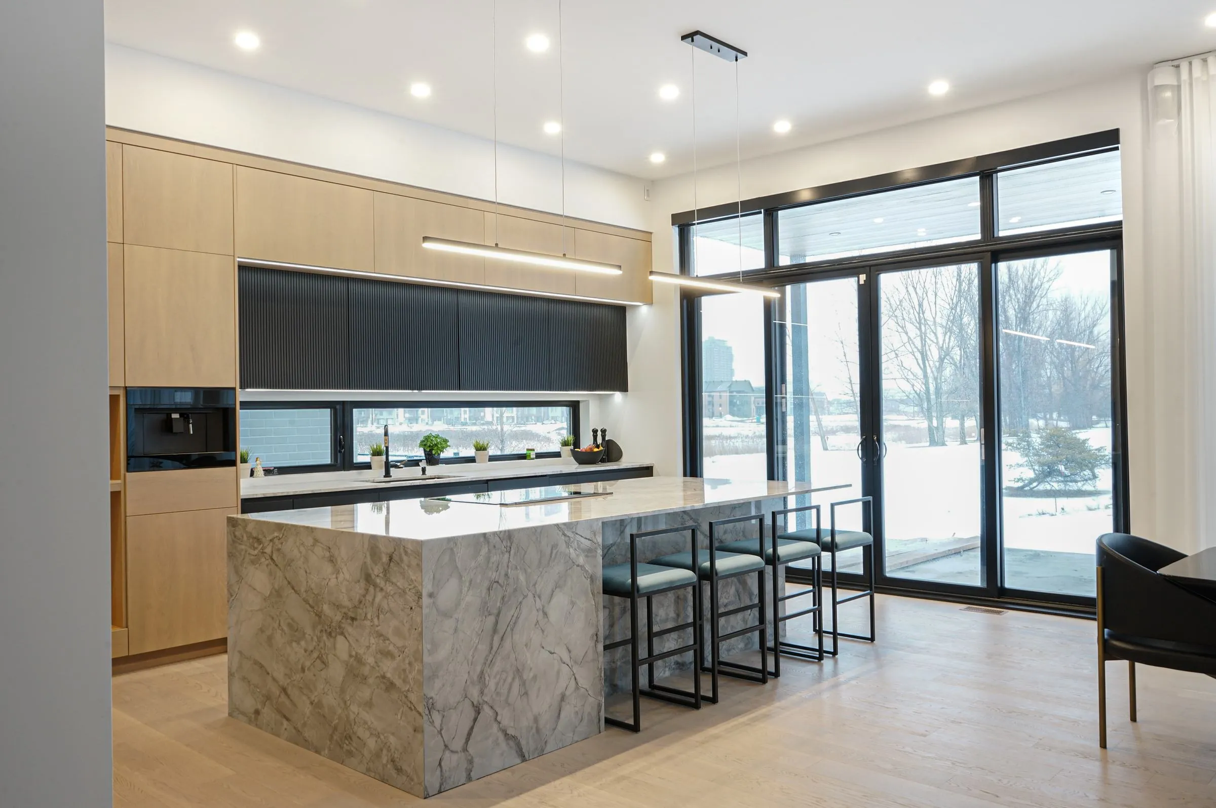 Contemporary kitchen with a marble island, pale wood cabinetry and floor to ceiling windows