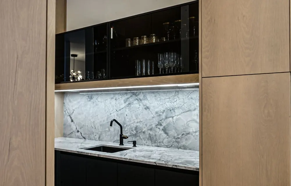Wet bar with a marble backsplash and pale wood cabinetry